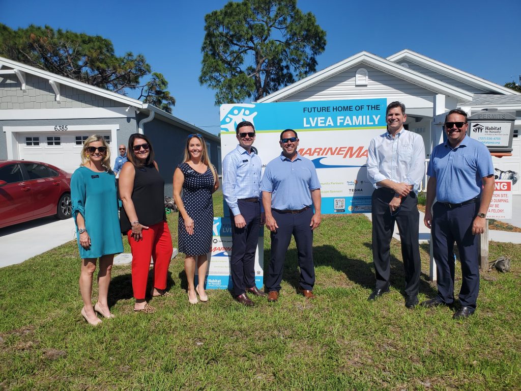 Marine Max employees participating in Habitat for humanity - standing in front of sign on a lawn.