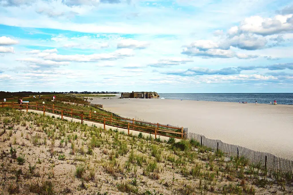 A sunny but slightlyt cloudy day at Cape May Beach with sand and ocean as the backdrop and a walkway on a sand dune heading to the waterfront.