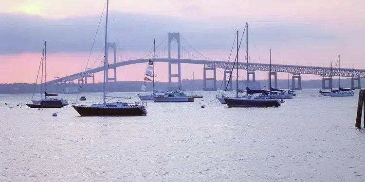 A pink sunset and bridge in the background while boats anchor in Narragansett Bay