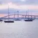 A pink sunset and bridge in the background while boats anchor in Narragansett Bay