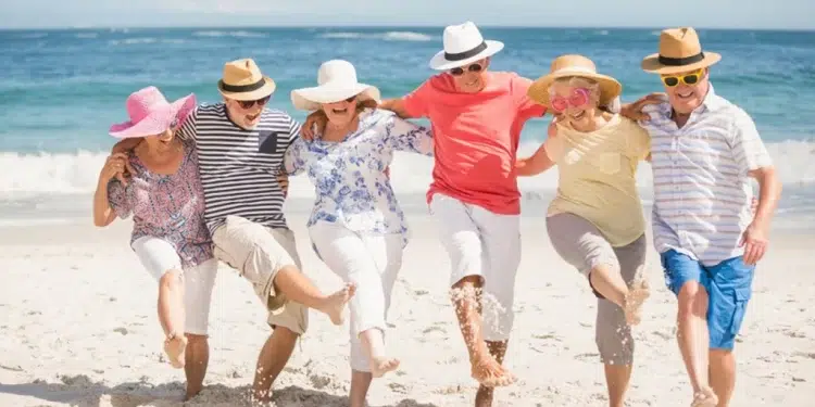 A mixed group of six holding arms kicking sand at the beach in joyful spirit