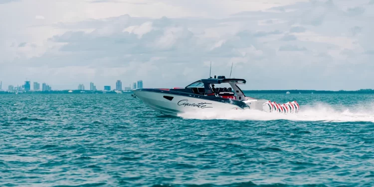 A side view of Cigarette Racing's boat cutting across water with a city skyline in the far distance