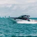 A side view of Cigarette Racing's boat cutting across water with a city skyline in the far distance