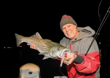 An angler holds his catch with a nighttime backdrop after fishing shadow lines