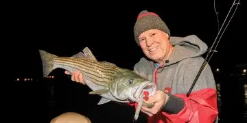 An angler holds his catch with a nighttime backdrop after fishing shadow lines