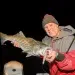 An angler holds his catch with a nighttime backdrop after fishing shadow lines