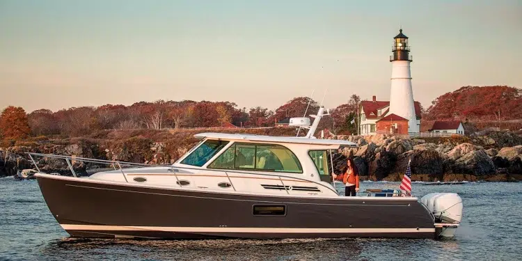 A side profile of the Back Cove 390 yacht at rest in water with a lighthouse and trees as the background