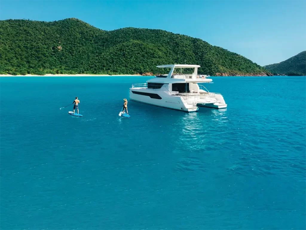 Two people paddle boarding by their catamaran