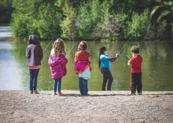 Five children face a lake as they learn to fish.