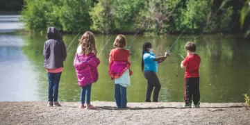 Five children face a lake as they learn to fish.