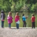Five children face a lake as they learn to fish.