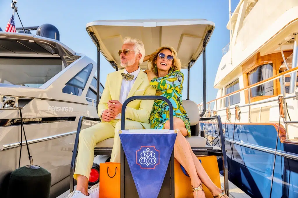 A couple dressed for summer weather sits on a golf cart as they head to their yacht at the town of Palm Beach marina