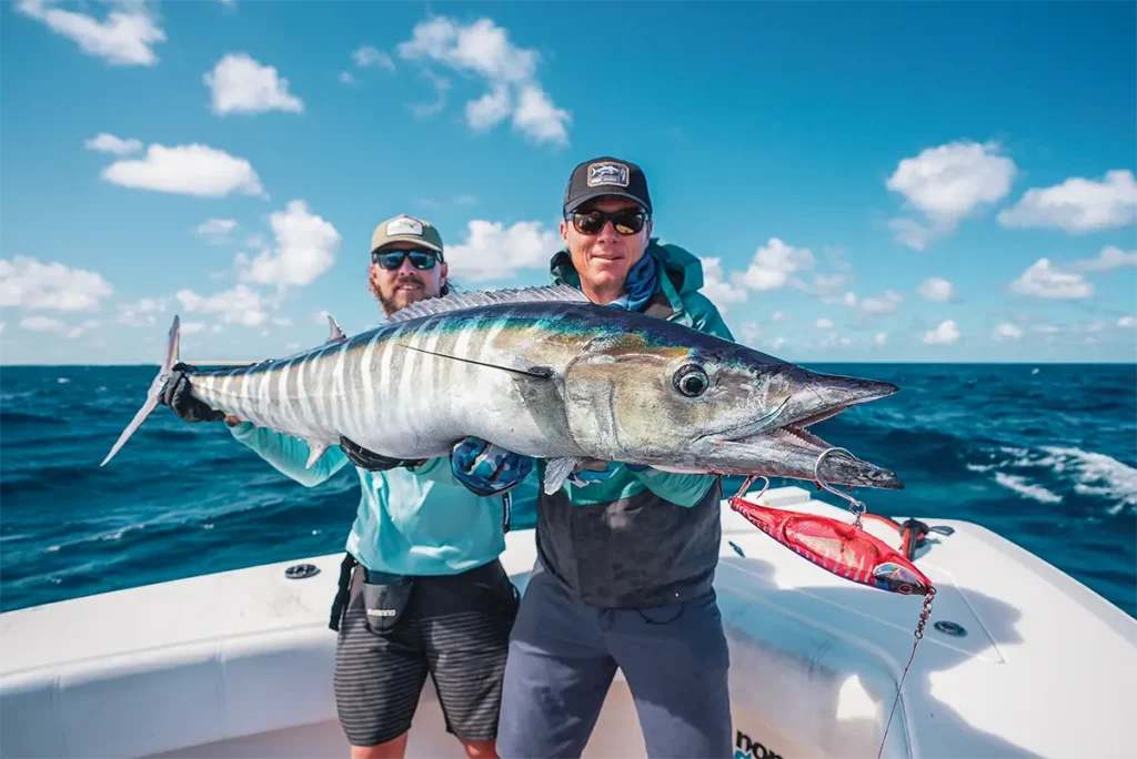 Two anglers holding up a huge wahoo fish on a boat.
