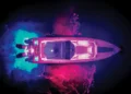 aerial shot of boat in the water at night lit up in rainbow colors with LED lights