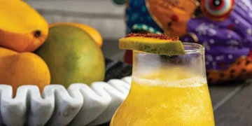Mango pisco cocktail garnished with mango slice and microgreens