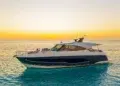 Riviera 5600 Sport Yacht lying at anchor at sunset with a guest relaxing on the bow lounge