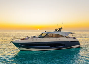 Riviera 5600 Sport Yacht lying at anchor at sunset with a guest relaxing on the bow lounge