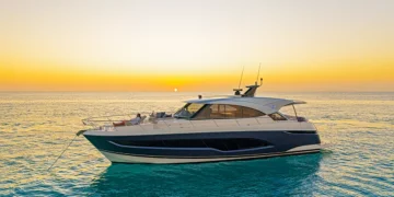 Riviera 5600 Sport Yacht lying at anchor at sunset with a guest relaxing on the bow lounge