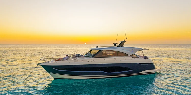 Riviera 5600 Sport Yacht lying at anchor at sunset with a guest relaxing on the bow lounge