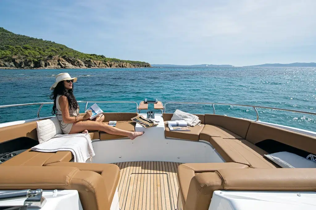 Guest reading on the Jeanneau TH38 bow lounge with sunpad cushions and a teak-floored center well